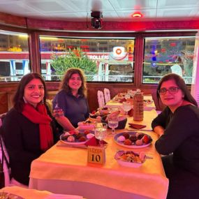Three women enjoying dinner on a cruise with city lights outside.