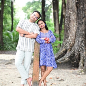 A couple posing together in a forested area, leaning on a post