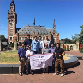A group of men posing with a banner in front of a historic building.