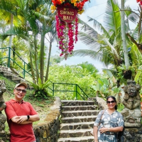 Couple posing at 'My Swing Bali' amid lush greenery and statues.