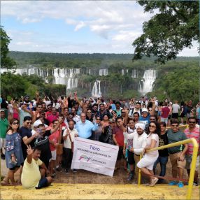 A large group posing with a banner at a scenic waterfall location.