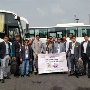 Group of People posing with a welcome banner near buses.