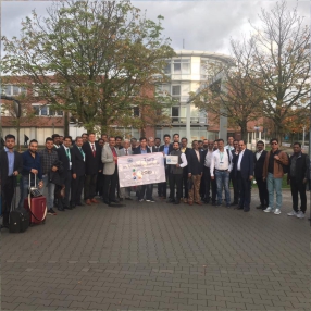 A large group of professionals posing outdoors with a banner.