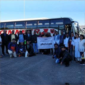 Large group posing with a 'Photokina' banner near a bus.