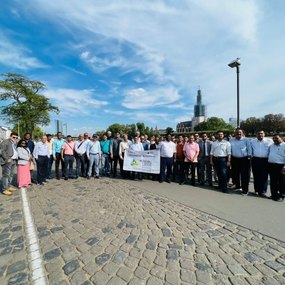 Large group posing outdoors on a cobblestone path with a banner.