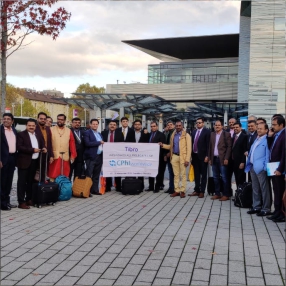 Delegation posing with a banner outside a modern glass building.
