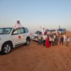 A group of people stands in the desert beside their vehicles 