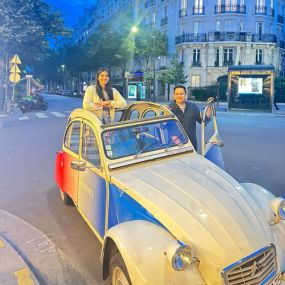 Two women posing with a vintage French car on a Paris street.