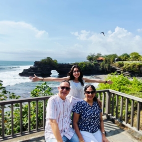 A family enjoys a scenic coastal view with smiles and open arms.